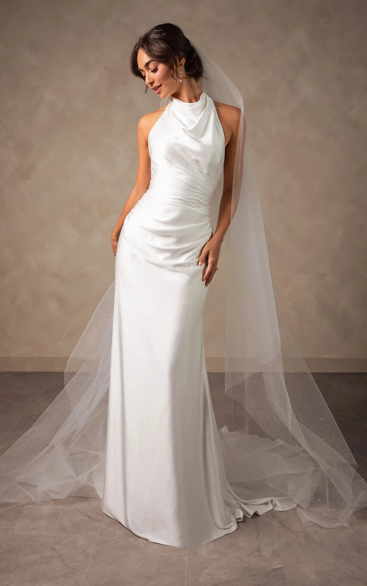Woman wearing a white wedding dress with a long train against a neutral background